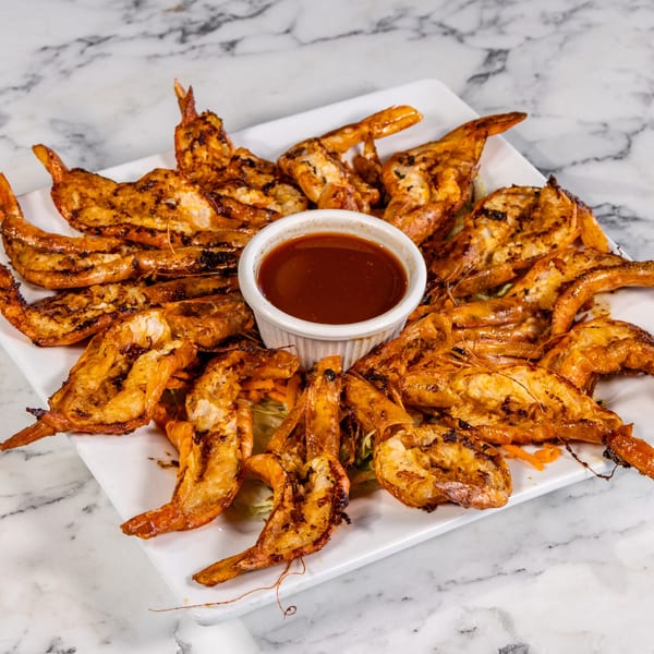 Grilled shrimp arranged around a small white bowl of red dipping sauce on a white plate.