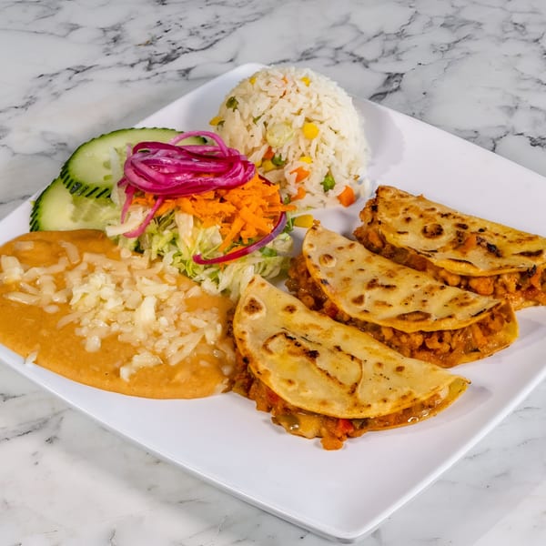 Mexican dish with three tacos, rice, refried beans, salad, and cucumber slices on a white plate.