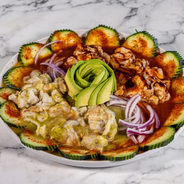 A Mexican seafood dish with shrimp, avocado, red onion, and cucumber slices on a white plate.