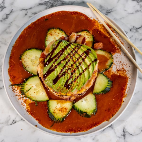 Mexican seafood tower with avocado, shrimp, and cucumbers in a red sauce, with chopsticks.
