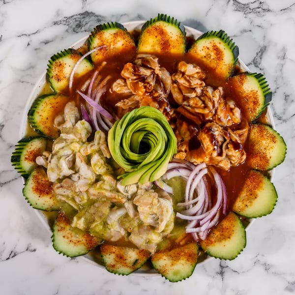 A vibrant Mexican seafood platter with shrimp, red onions, cucumber slices, and avocado on marble.