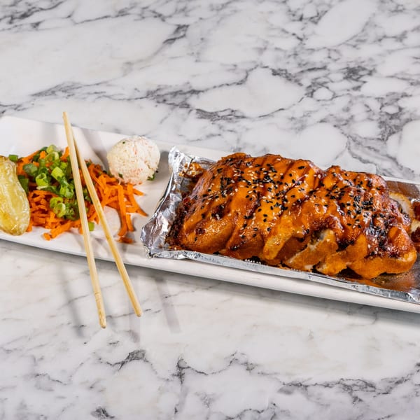 Baked sushi roll with orange sauce and sesame seeds, served with rice, carrots, and green onions.