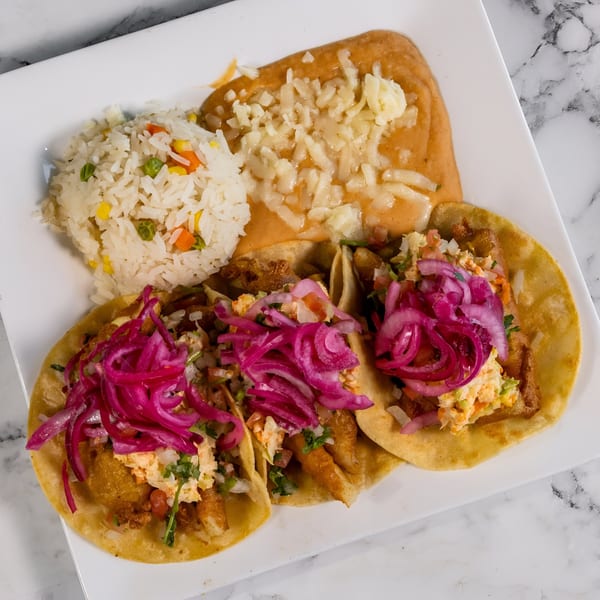 Three Mexican tacos with pickled red onions, rice, and refried beans with cheese on a white plate.